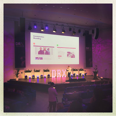 Totales Bild der lila eingeleuchtete Bühne mit Speaker auf der DRX Düsseldorf 2024