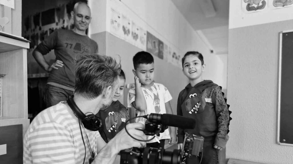 Making-of-Bild bei den Dreharbeiten zu der Recruiting Video Serie für 'Die Bildungspartner'. DAS GUTE WERK zeigt Kind die Filmausrüstung, ein Junge schaut sich die Kamera genauer an.