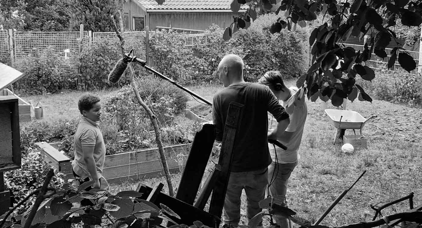 Making-of-Bild bei den Dreharbeiten zu der Recruiting Video Serie für 'Die Bildungspartner'. DAS GUTE WERK spricht mit einem Kind im Schulgarten, während es gefilmt wird.